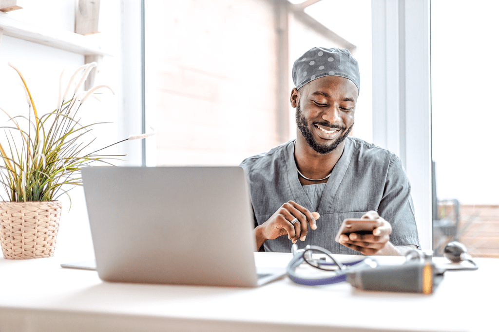 Healthcare Profession Sitting at His Desk, Smiling and Looking at Phone to Use for Digital Ordering Food