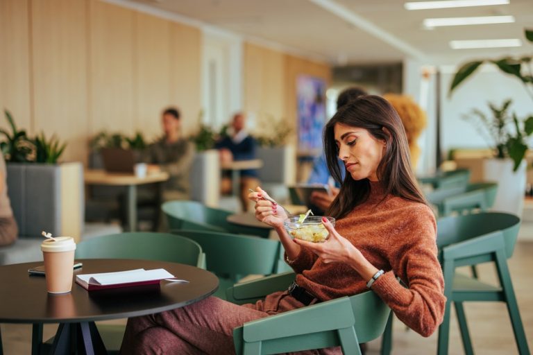 A young adult Caucasian businesswoman is eating breakfast in the company cafeteria.
